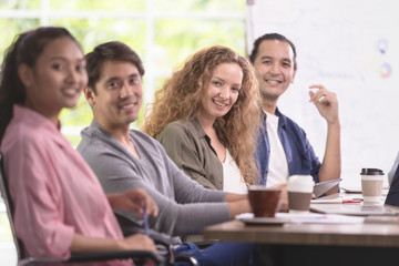 Group of Asian and caucasian businessmen is meeting his work. And happily smile at their job. In the modern office. There is poster board behind.