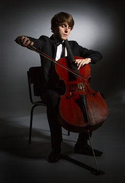 Young man playing the cello. Portrait of the cellist on a dark background.