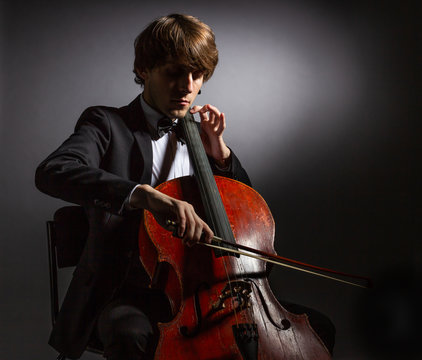 Young man playing the cello. Portrait of the cellist on a dark background.