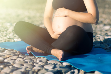 Fototapeta na wymiar Young pregnant woman doing yoga exercises on the beach