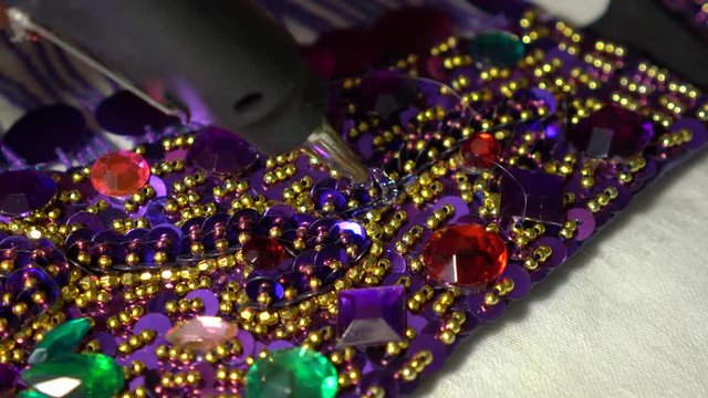 Closeup of woman&rsquo;s fingers holding a clear jewel into place, pulling it away, using a glue gun to put hot glue, and then pressing the rhinestone into place.
