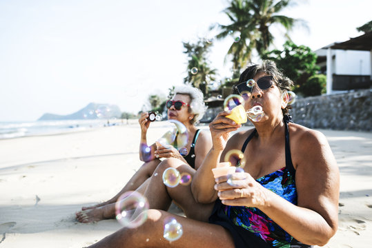 Senior friends blowing bubble and chilling on the beach