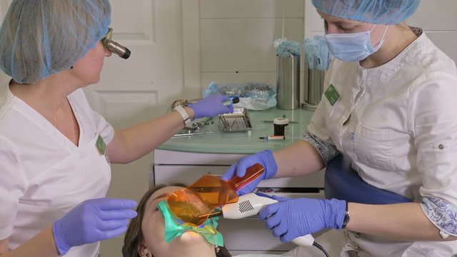 Woman at dentist clinic gets dental treatment to fill a cavity in a tooth. Dental restoration and composite material polymerization with UV light and laser. The doctor works with an assistant.