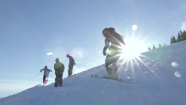 Group of skiers, skiing up a hill while the sun backlights them creating lens flares in the camera.