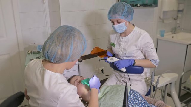 Woman at dentist clinic gets dental treatment to fill a cavity in a tooth. Dental restoration and composite material polymerization with UV light and laser. The doctor works with an assistant.