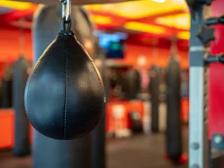 Fotobehang Black leather speedbag, with Muay Thai bags in the back, ready for use in a gym © David Tran