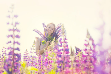 Obraz na płótnie Canvas Beautiful and happy woman with bouquet of lupines on the field