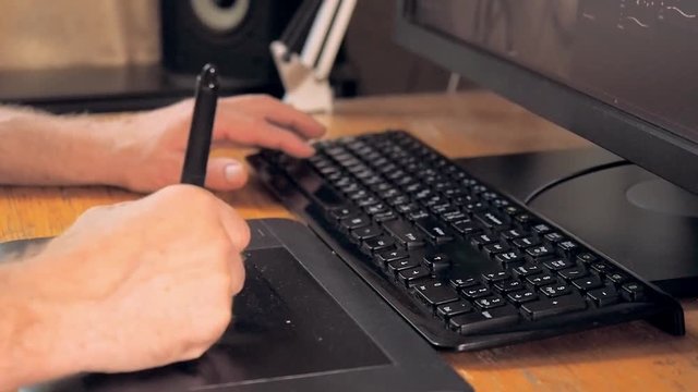 Graphic designer drawing on tablet computer with digital pen, close up view. Man's hand using touch screen pen and black keyboard. Man at work on tablet PC. Blurred background, soft selective focus