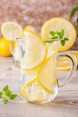 Refreshing mineral water with lemon, mint and ice cubes in glasses on a wooden table