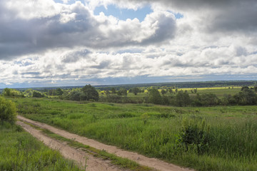 Dirt road with deep against cloudy sky background.
