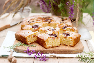 Pieces of fruit pie with pieces of plums and peach and a bouquet of flowers on a wooden table. Rustic style.