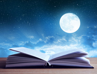 Open book on wooden plank night sky with moon in the background. 