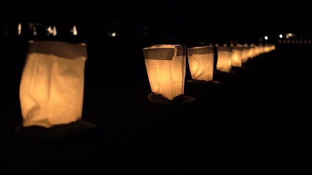 Christmas Eve candle lights flame closeup illuminated in paper bags on plates at night in row lining street road by residential neighborhood house decoration during holiday