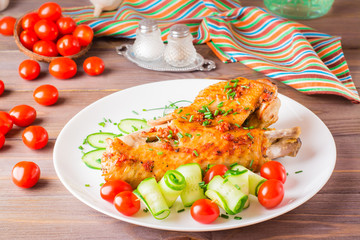 Baked turkey wing, cucumber slices and cherry tomatoes on a plate on a wooden table