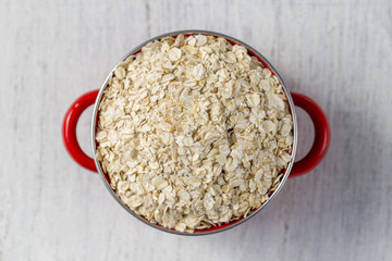 Red pan with dry oat flakes on white old wooden background. Closeup. Concept healthy eating