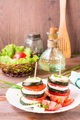 Original appetizer from fried zucchini, fresh tomatoes and feta cheese on a wooden skewer on a white plate
