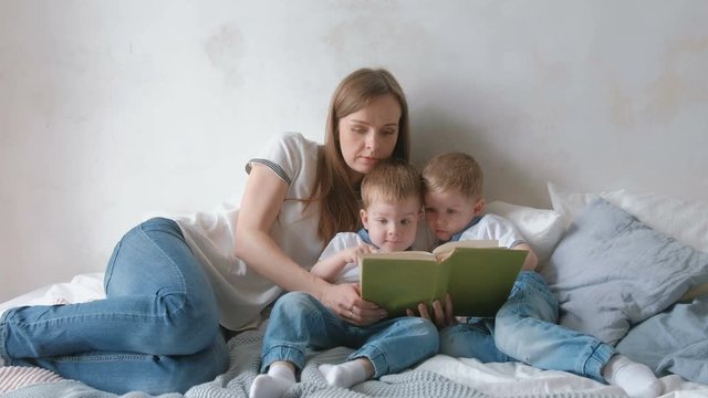 Family mom and two twin brothers toddlers read books laying on the bed. Family reading time.