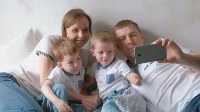 Dad makes family selfie on mobile phone. Mom, dad and two brother twins toddlers.