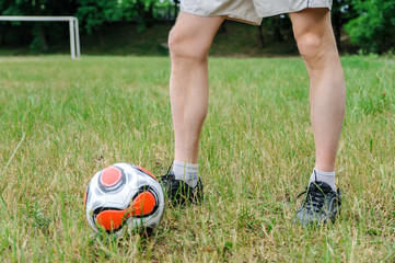Men's legs are on the grass. There is a soccer ball next to it.
