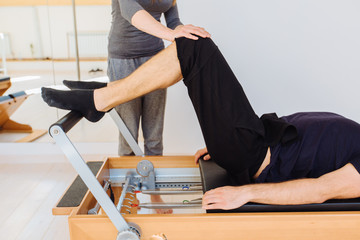 Female instructor with cute braids hairstyle consulting unrecognizable man workout pilates on...