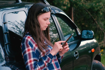 Naklejka premium Woman sends a message on the phone standing next to the car.