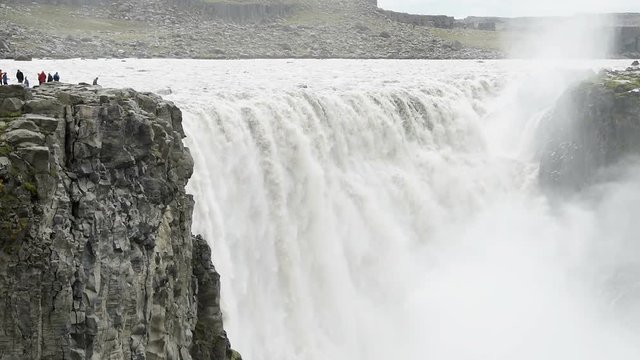 Iceland Dettifoss waterfall, largest volume in Europe closeup, people on cliff top, gray grey water, rocky cliff and water flowing, mist spraying