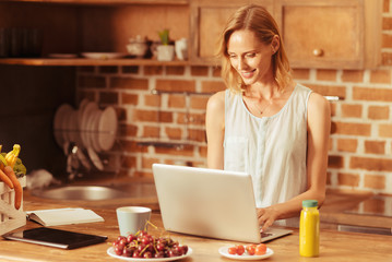 Online chat. Delighted woman keeping smile on her face and bowing head while looking at computer