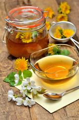 Dandelion honey, spring flowers, spoon, dandelion head around, small colander and full jar in background - vertical photo