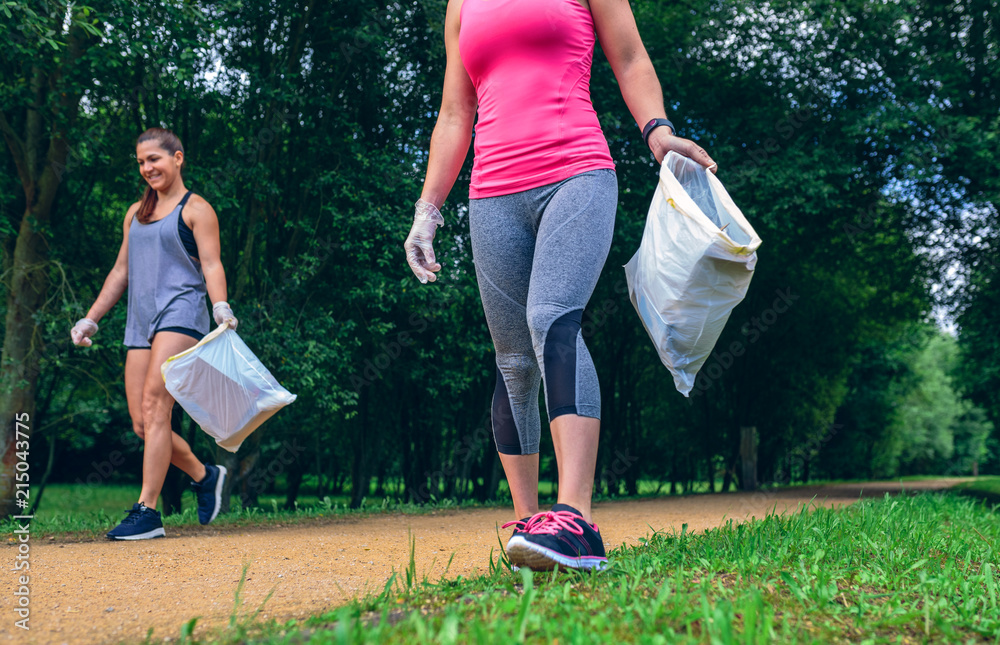 Wall mural happy girls with garbage bag picking up trash doing plogging