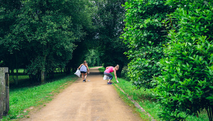 Fototapeta premium Two girls on back with garbage bags doing plogging