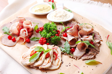 Meat appetizer on wooden board: bacon, beef tongue and others with greens and sauce