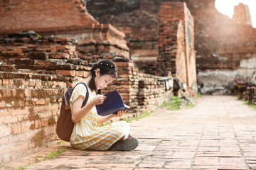 Asian cute girl relaxing outdoors while read history book,Student enjoy learning at historical, park,Wat Mahathat,Ayutthaya,Thailand - obrazy, fototapety, plakaty