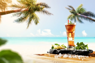 Fresh cold ice tea drink on table and landscape of beach with two palms. 