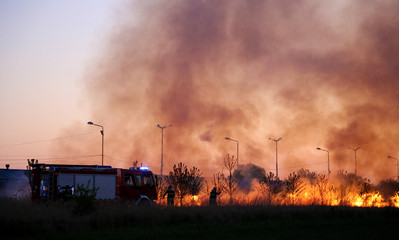 Team of fire fighters fighting fire in the evening. Fire truck on the flames and smoke background.