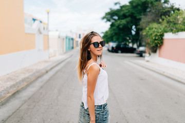 Beautiful young woman in sunglasses walking on the summer street