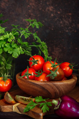 Fresh tomatoes and parsley, dill, garlic on a dark background in a rustic kitchen and wooden utensils still life with copy space