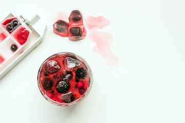 Cocktail of berries frozen in ice cubes (raspberries, blackberries , red and black currants) . Summer cold refreshing drink. Selective focus.Copy space.