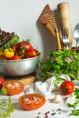 Fresh tomatoes and parsley, dill, garlic on a light background in a rustic kitchen and wooden utensils still life with a copy space