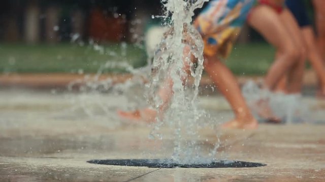 Closeup up of child's feet playing and running through fountain in public park. Shallow depth of the field, toned video, 50fps.