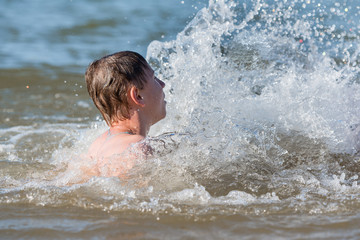 A boy teen swims in a spray of water - a concept of a beach holiday