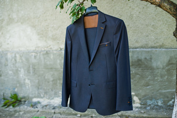 Close-up photo of groom's jacket hanging on the tree branch outdoors.