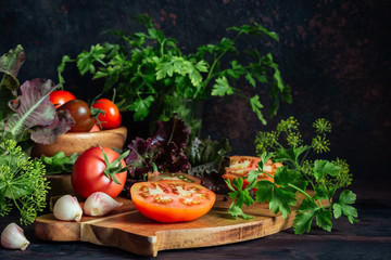 Fresh tomatoes and parsley, dill, garlic on a dark background in a rustic kitchen and wooden utensils still life with copy space