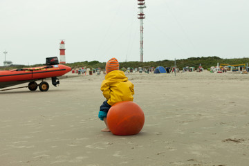 kid hops on red jumping ball on the beach