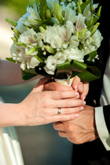 women's and men's hands with wedding rings, hold a bouquet
