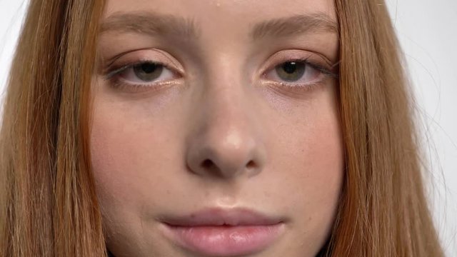 Face of young sweet calm ginger girl is watching at camera, white background