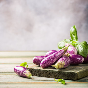 Heap of small eggplant or aubergine vegetable with basil leaves on old wooden background. Healthy food concept with copy space.