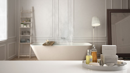 Spa, hotel bathroom concept. White table top or shelf with bathing accessories, toiletries, over blurred scandinavian bathroom, modern architecture interior design