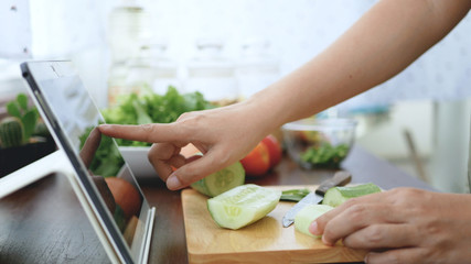 Aziatische vrouw gebruikt vingerdia op tabletscherm bereid ingrediënten voor om te koken, volg de online videoclip op de website. kookinhoud op internettechnologie voor modern lifestyle-concept
