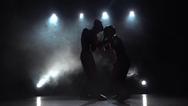 Girl is kicking the guy they are sparring for kickboxing . Smoke background. Silhouette. Slow motion