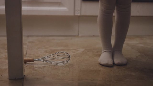 Close up of the kid's barefeet in white tights standing in the kitchen and kitchen stuff falling on the floor. Indoors